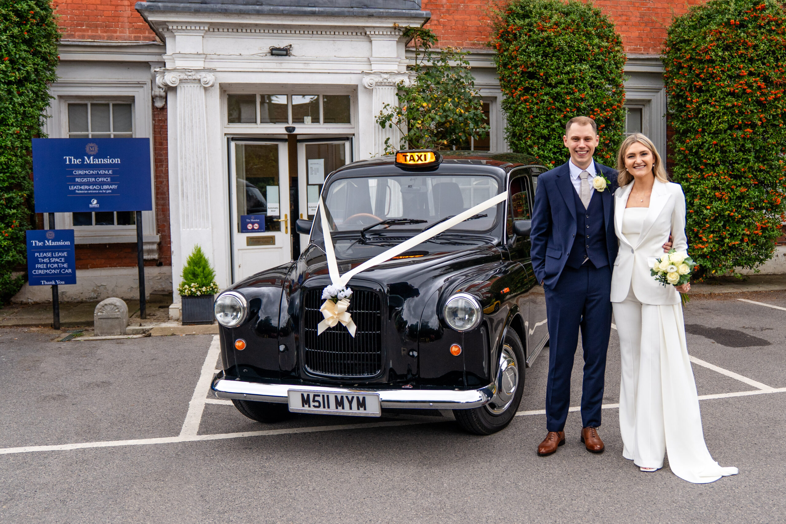 Bride and groom in the front of Leatherhead registry office with taxi