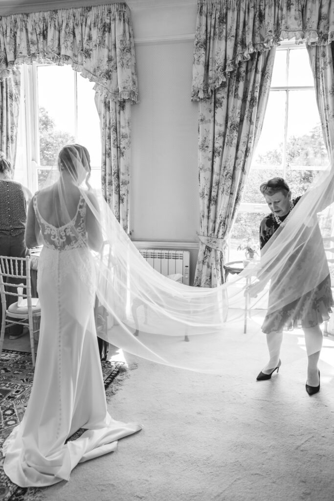 Bride putting on her dress in a high-ceilinged country estate suite, captured by a Buckinghamshire wedding photographer.