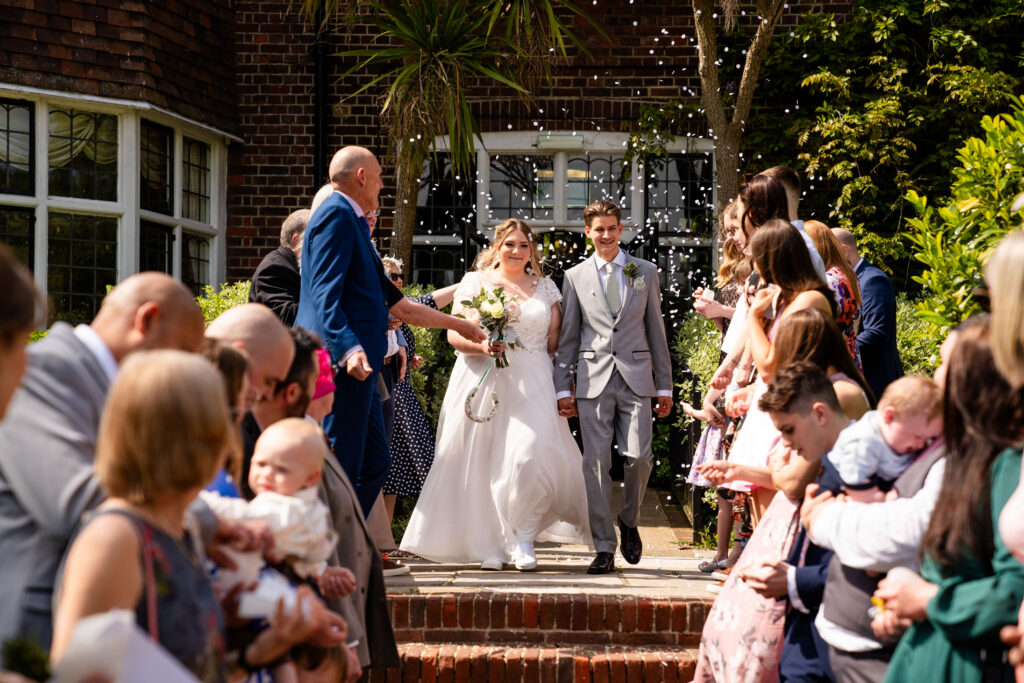 Wedding guests throwing dried flower confetti high into the air over a couple walking down the aisle.