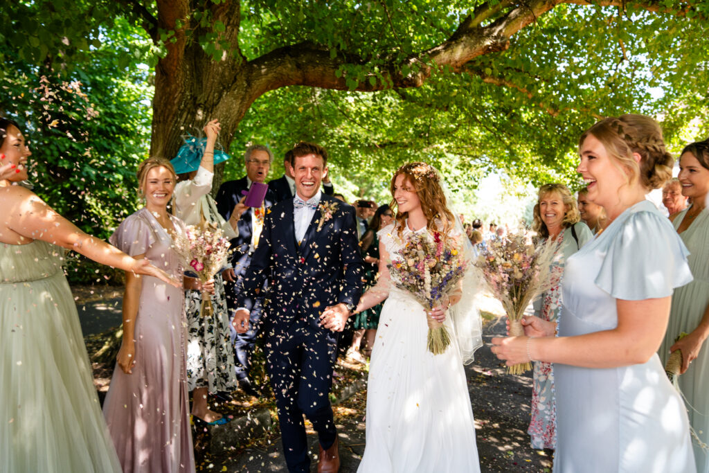 Newly married couple walking down the aisle surrounded by a cloud of colorful wedding confetti in London.